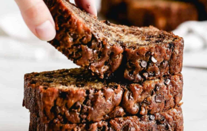 A sliced loaf of moist homemade banana bread on a wooden board with caramelized bananas on top