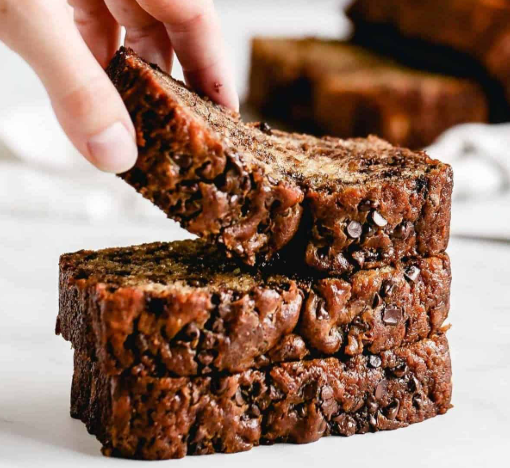 A sliced loaf of moist homemade banana bread on a wooden board with caramelized bananas on top