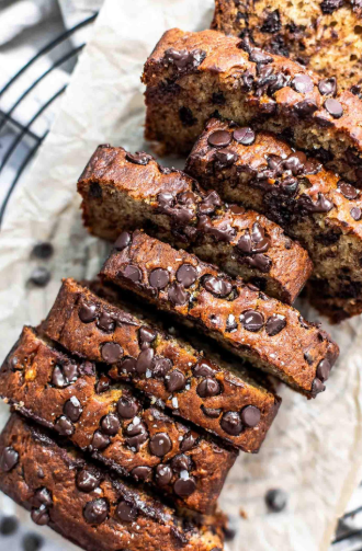 A sliced loaf of moist homemade banana bread on a wooden board with caramelized bananas on top