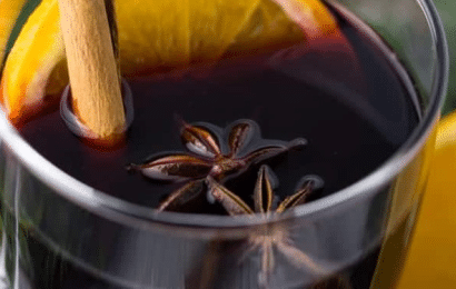 A glass mug filled with steaming German Mulled Wine Recipe garnished with an orange slice and cinnamon stick.