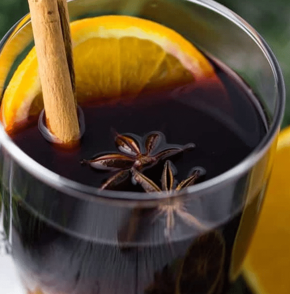 A glass mug filled with steaming German Mulled Wine Recipe garnished with an orange slice and cinnamon stick.