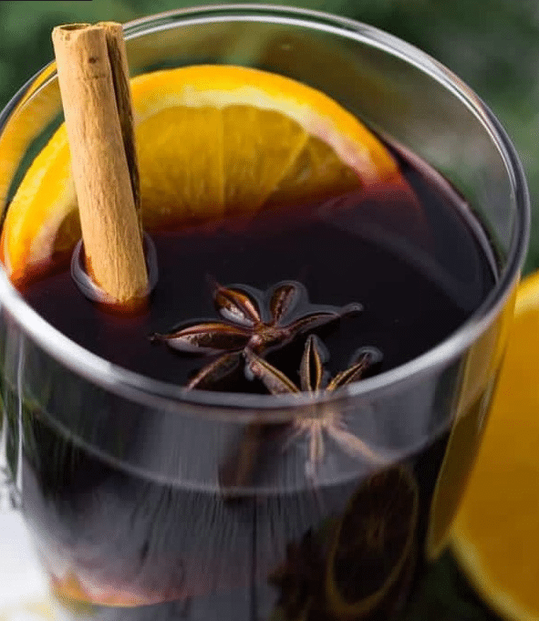 A glass mug filled with steaming German Mulled Wine Recipe garnished with an orange slice and cinnamon stick.