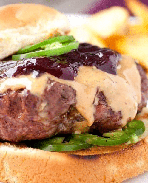 A juicy Peanut Butter Jelly Burger with melted peanut butter and crispy bacon on a toasted bun