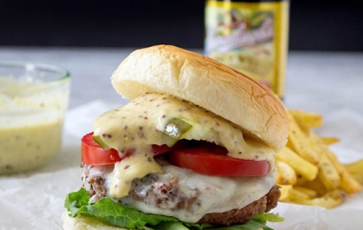A giant Smoky Beer Burger topped with melted gouda cheese, crispy bacon, and caramelized onions on a brioche bun