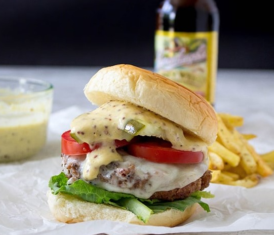 A giant Smoky Beer Burger topped with melted gouda cheese, crispy bacon, and caramelized onions on a brioche bun