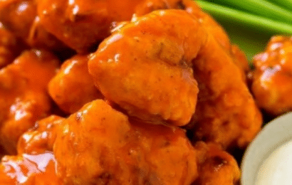 A platter of crispy buffalo chicken nuggets served with celery sticks and ranch dipping sauce.