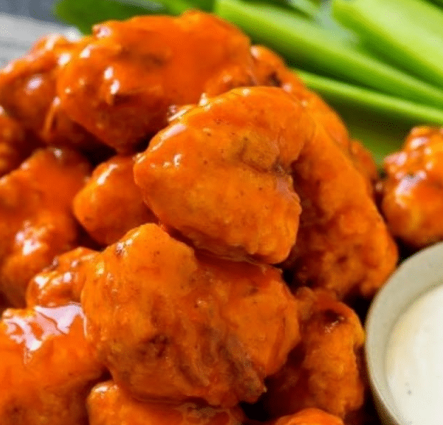 A platter of crispy buffalo chicken nuggets served with celery sticks and ranch dipping sauce.