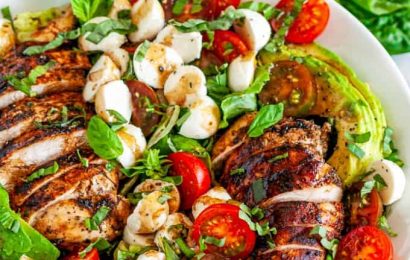A large white bowl filled with Chicken Caprese Salad featuring cherry tomatoes, mozzarella pearls, and sliced grilled chicken.