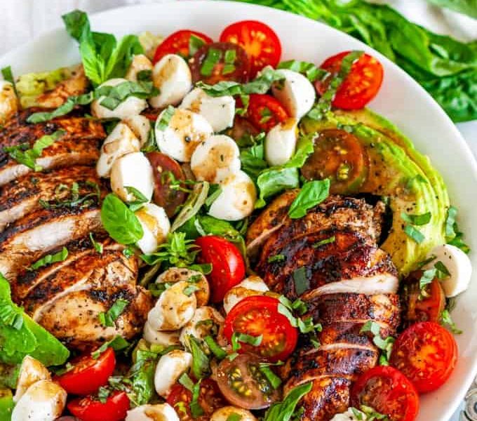 A large white bowl filled with Chicken Caprese Salad featuring cherry tomatoes, mozzarella pearls, and sliced grilled chicken.