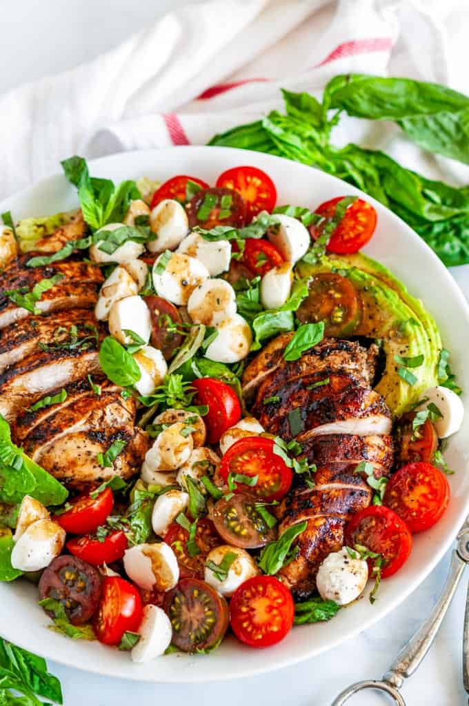 A large white bowl filled with Chicken Caprese Salad featuring cherry tomatoes, mozzarella pearls, and sliced grilled chicken.