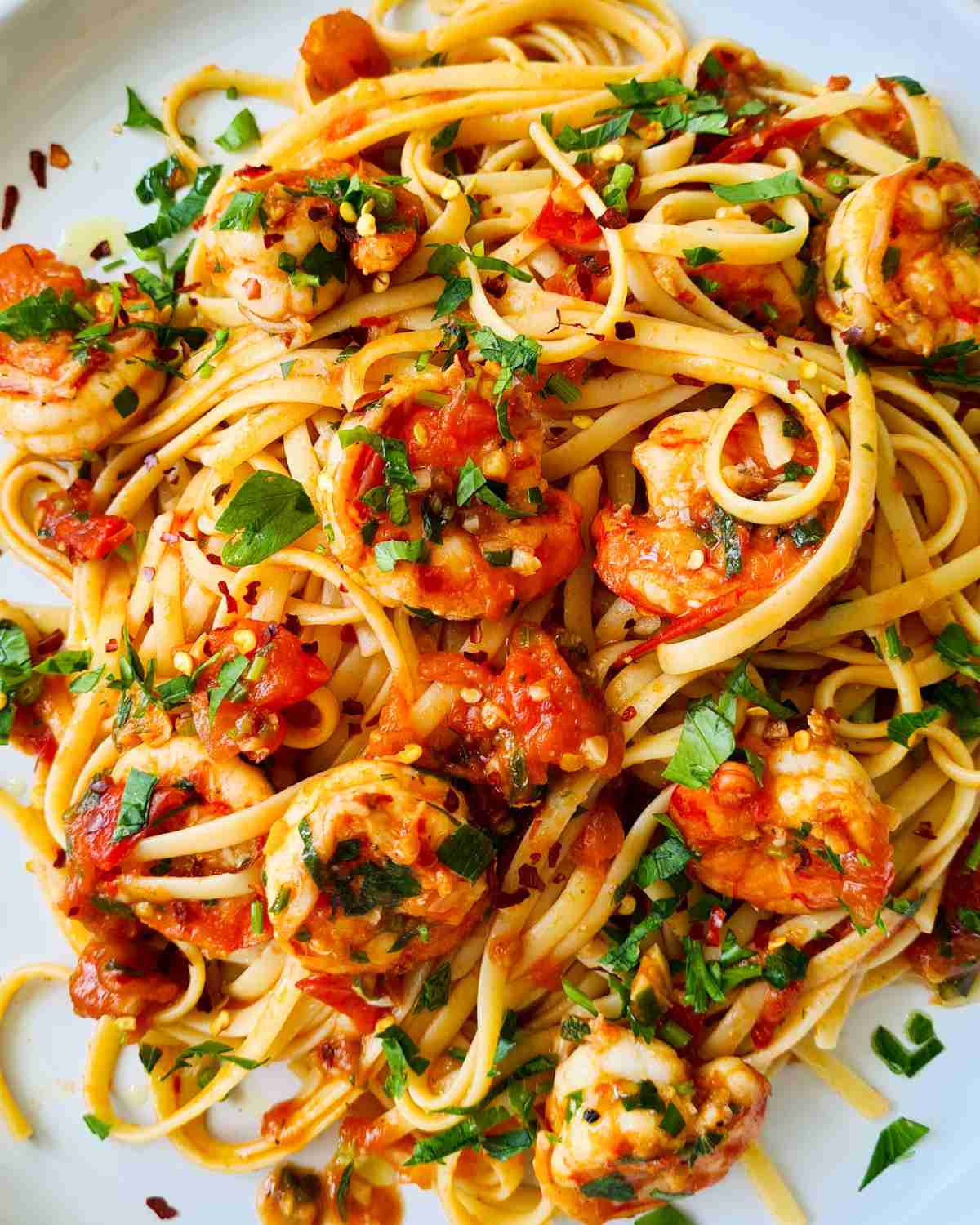 A bowl of Chilli and Prawn Linguine topped with fresh parsley and lemon wedges.