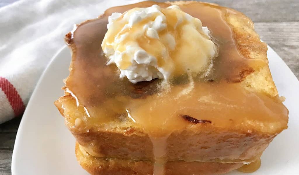 Stack of Copycat Kneaders Chunky Cinnamon French Toast topped with whipped cream and caramel syrup