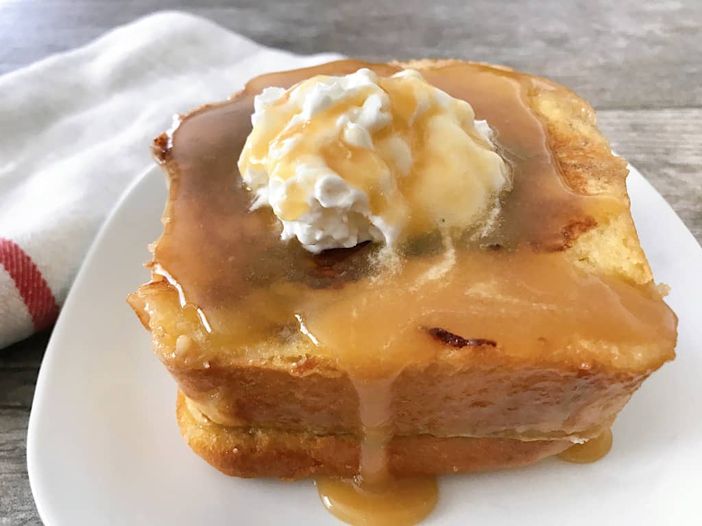 Stack of Copycat Kneaders Chunky Cinnamon French Toast topped with whipped cream and caramel syrup