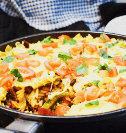 A steaming bowl of Easy Taco Pasta Recipe topped with melted cheese and fresh spring onions.