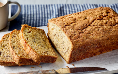 A freshly baked loaf of moist banana bread topped with caramelized banana slices on a rustic wooden board