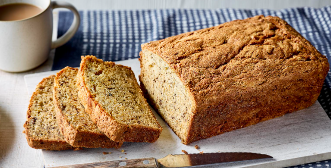 A freshly baked loaf of moist banana bread topped with caramelized banana slices on a rustic wooden board