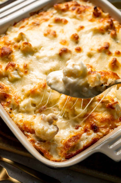 A golden-brown baked cauliflower cheese in a white ceramic dish with bubbling rich cheese sauce