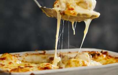 A golden-brown baked cauliflower cheese in a white ceramic dish with bubbling rich cheese sauce