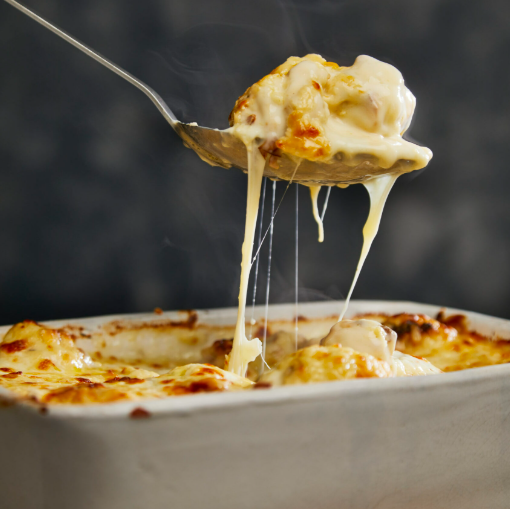 A golden-brown baked cauliflower cheese in a white ceramic dish with bubbling rich cheese sauce