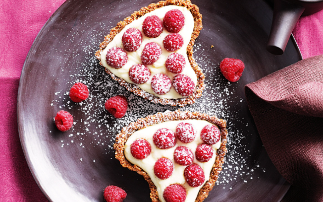 A romantic candlelit table featuring heart-shaped pizza, sparkling wine, and chocolate-covered strawberries for Valentine's Day