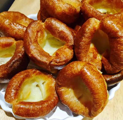 Pouring smooth Yorkshire pudding batter from a glass jug into a smoking hot muffin tin.