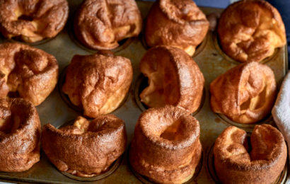 A stack of tall, golden homemade Yorkshire puddings served on a white plate with gravy