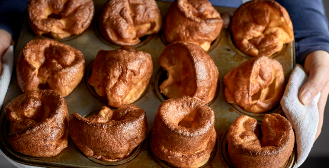 A stack of tall, golden homemade Yorkshire puddings served on a white plate with gravy