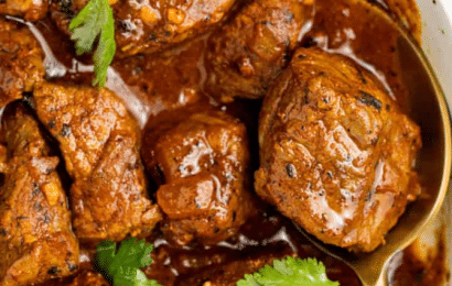 A bowl of rich, red Beef Vindaloo garnished with fresh cilantro, served alongside fluffy basmati rice and warm garlic naan