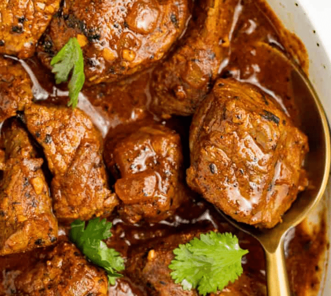 A bowl of rich, red Beef Vindaloo garnished with fresh cilantro, served alongside fluffy basmati rice and warm garlic naan