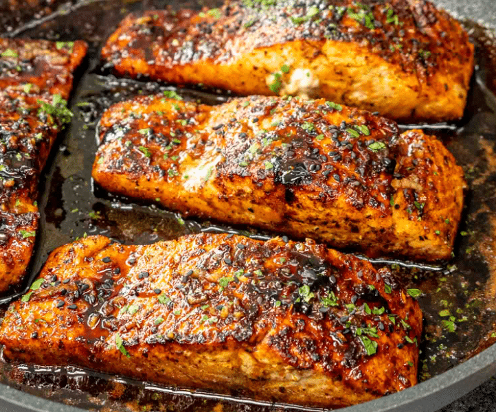 A pan-seared salmon fillet glazed in a glossy honey butter sauce with charred lemon slices and fresh parsley.