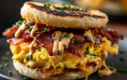A stacked, juicy Chipotle Breakfast Sandwich with a runny egg, crispy bacon, melted cheddar, and creamy spicy sauce on a toasted brioche bun.