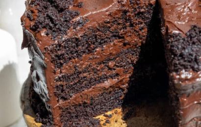 A towering, decadent four-layer Death by Chocolate Cake covered in rich chocolate buttercream, a glossy chocolate ganache drip, and topped with chocolate curls and truffles.