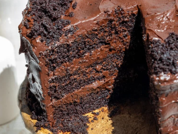 A towering, decadent four-layer Death by Chocolate Cake covered in rich chocolate buttercream, a glossy chocolate ganache drip, and topped with chocolate curls and truffles.