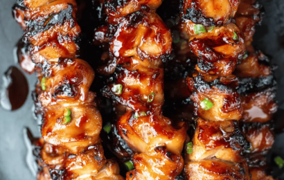 A platter of glossy, caramelized Filipino barbecue chicken skewers garnished with fresh scallions and charred lemon halves.