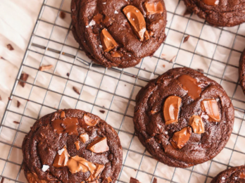 A stack of thick, fudgy double chocolate chip cookies on a cooling rack with melted chocolate puddles on top.