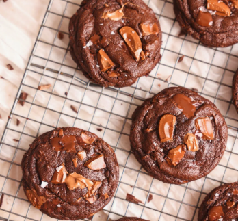 A stack of thick, fudgy double chocolate chip cookies on a cooling rack with melted chocolate puddles on top.