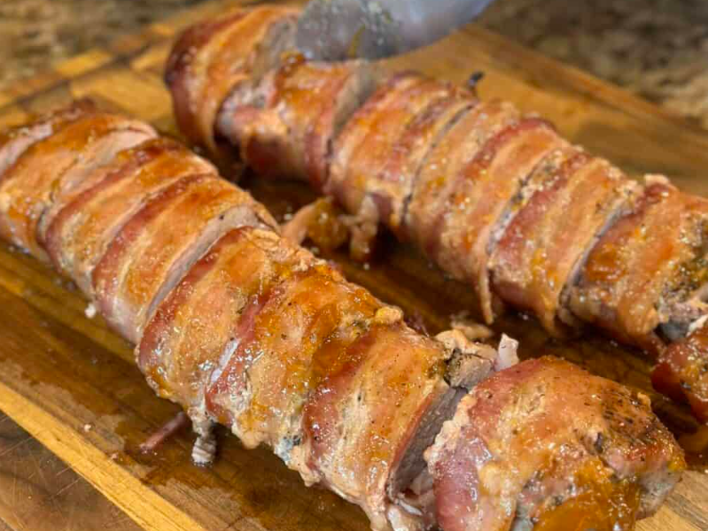 A perfectly sliced juicy roasted pork tenderloin coated in a sticky, golden brown sugar glaze, served on a white serving platter with a sprinkle of fresh parsley.