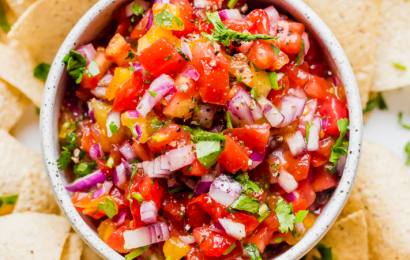 A rustic wooden bowl filled with chunky homemade salsa made with fresh tomatoes, cilantro, and onions, surrounded by tortilla chips.