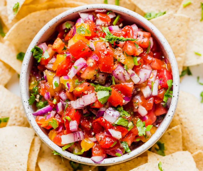 A rustic wooden bowl filled with chunky homemade salsa made with fresh tomatoes, cilantro, and onions, surrounded by tortilla chips.