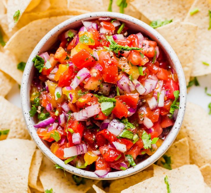 A rustic wooden bowl filled with chunky homemade salsa made with fresh tomatoes, cilantro, and onions, surrounded by tortilla chips.