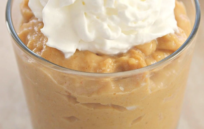 A close-up of a rich, creamy bowl of homemade spiced pumpkin pudding, generously topped with a dollop of fresh whipped cream and a sprinkle of cinnamon on a rustic wooden table.