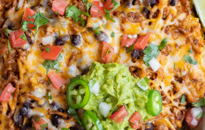 A large sheet pan piled high with crispy tortilla chips, melted cheese, seasoned shredded tofu, fresh jalapeños, and guacamole.