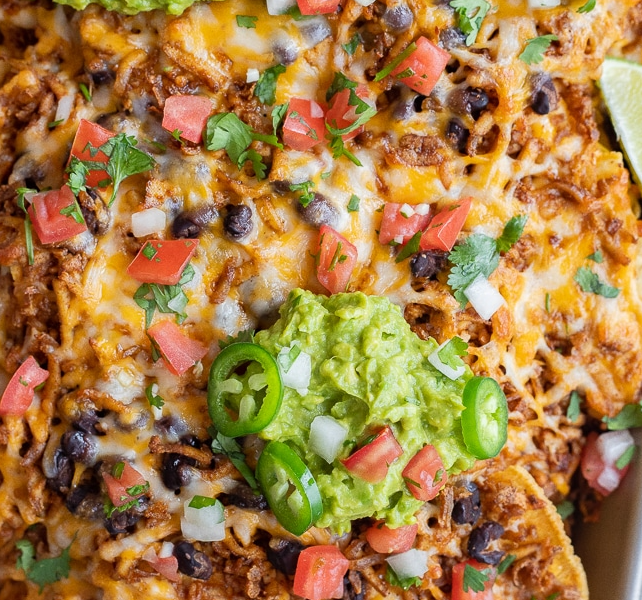A large sheet pan piled high with crispy tortilla chips, melted cheese, seasoned shredded tofu, fresh jalapeños, and guacamole.