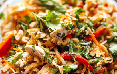 A colorful bowl of Chopped Thai-Inspired Chicken Salad with shredded purple cabbage, carrots, and diced chicken breast drizzled with peanut dressing.