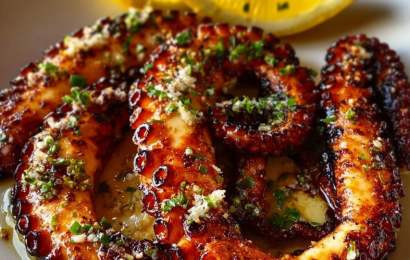 A beautifully charred Mediterranean grilled octopus tentacle served on a rustic plate, drizzled with olive oil, fresh lemon juice, capers, and chopped parsley.