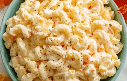 A large, beautiful bowl of creamy authentic Hawaiian macaroni salad mixed with fine orange carrot shreds and grated onions, served on a tropical wood table.