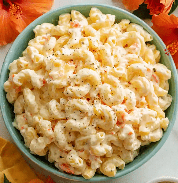 A large, beautiful bowl of creamy authentic Hawaiian macaroni salad mixed with fine orange carrot shreds and grated onions, served on a tropical wood table.