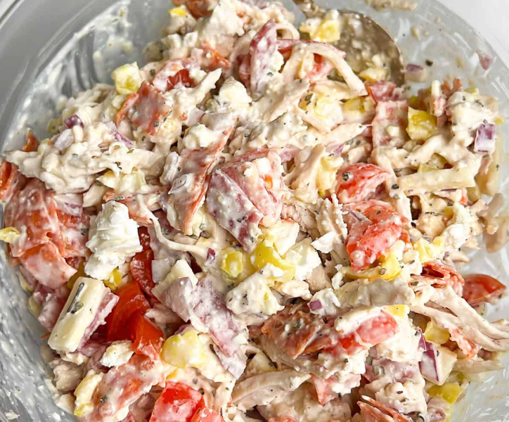 A large mixing bowl filled with creamy Italian grinder chicken salad, loaded with shredded chicken, chopped salami, pepperoncini, and finely shredded lettuce.