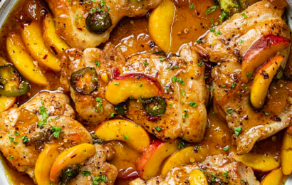 A hot cast-iron skillet featuring juicy pan-seared chicken breasts smothered in a glossy, golden peach glaze with sliced green jalapeños and fresh cilantro.