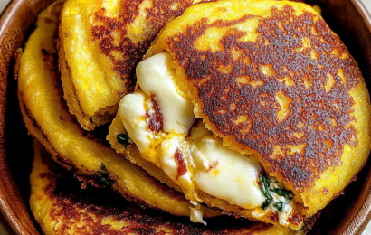 A steaming hot, golden-brown Venezuelan sweet corn cachapa folded in half, oozing with thick layers of melted white cheese on a rustic wooden board.